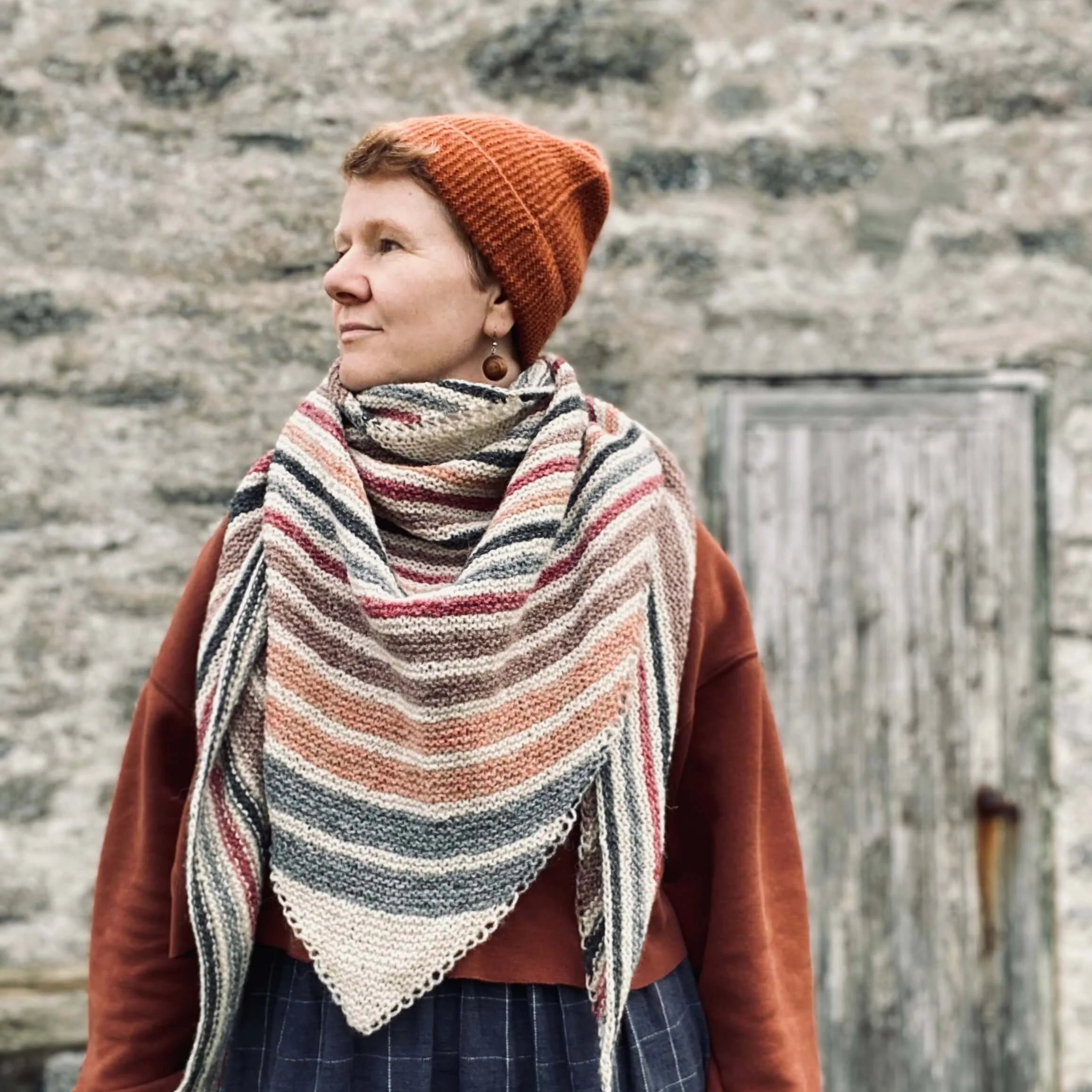 Gudrun Johnston wearing a striped shawl and orange beanie against a stone wall in Shetland..