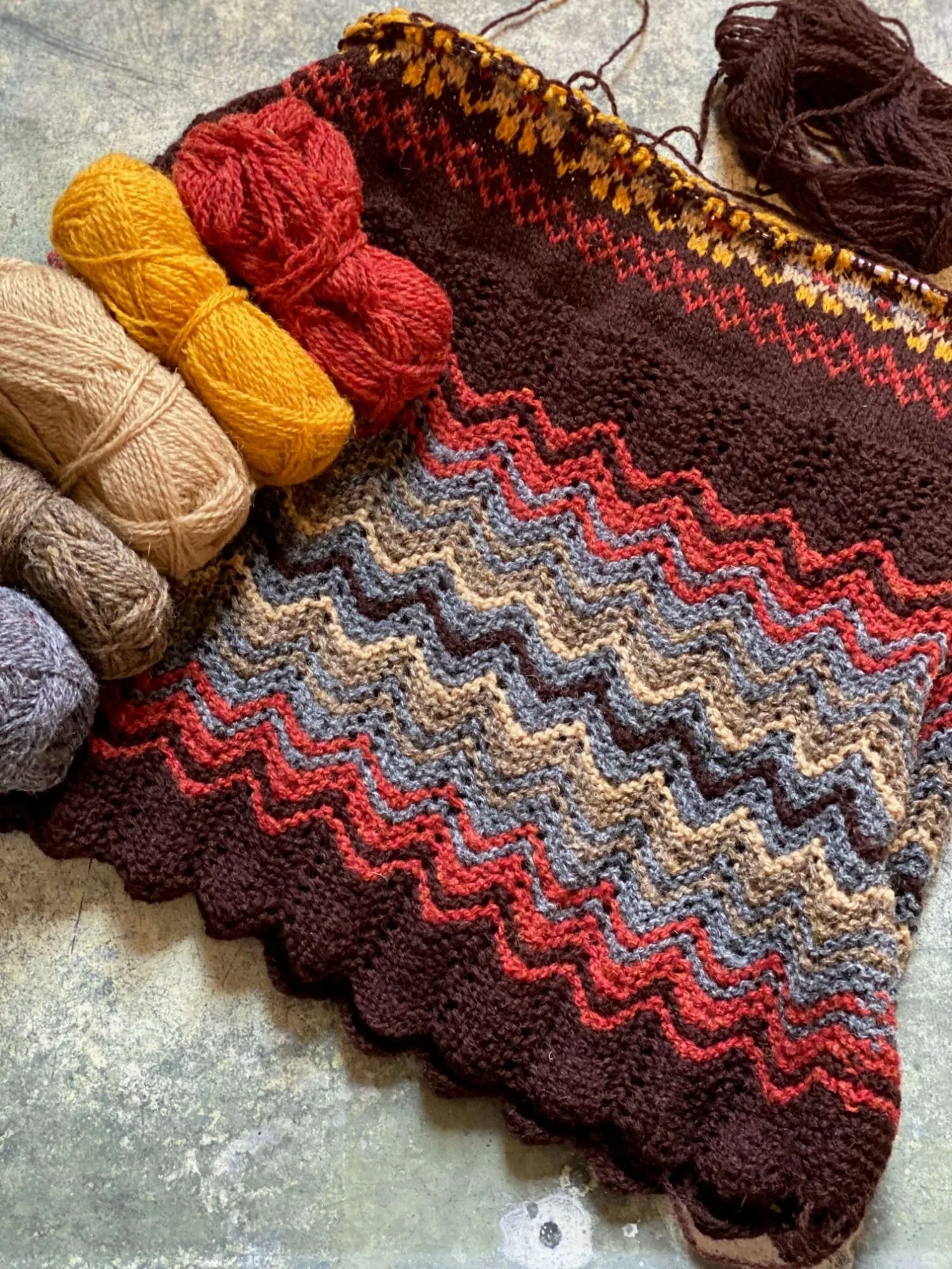 Knitted fabric with a Shetland shell lace pattern and colorful Jamieson's of Shetland yarn on a textured surface