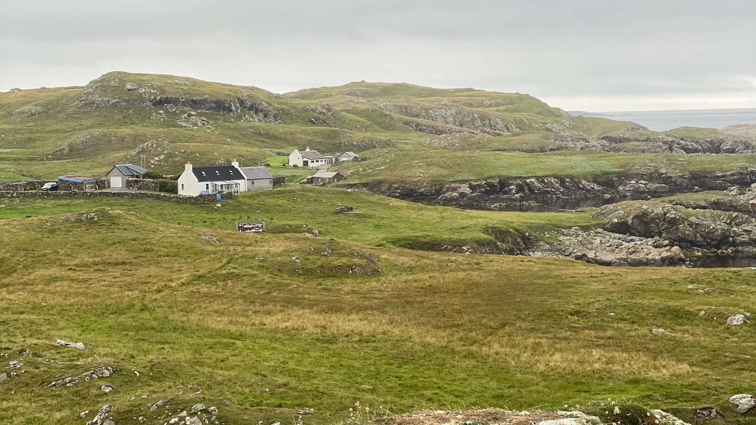 Scenic view of a rural landscape with houses on a grassy hillside in Shetland.