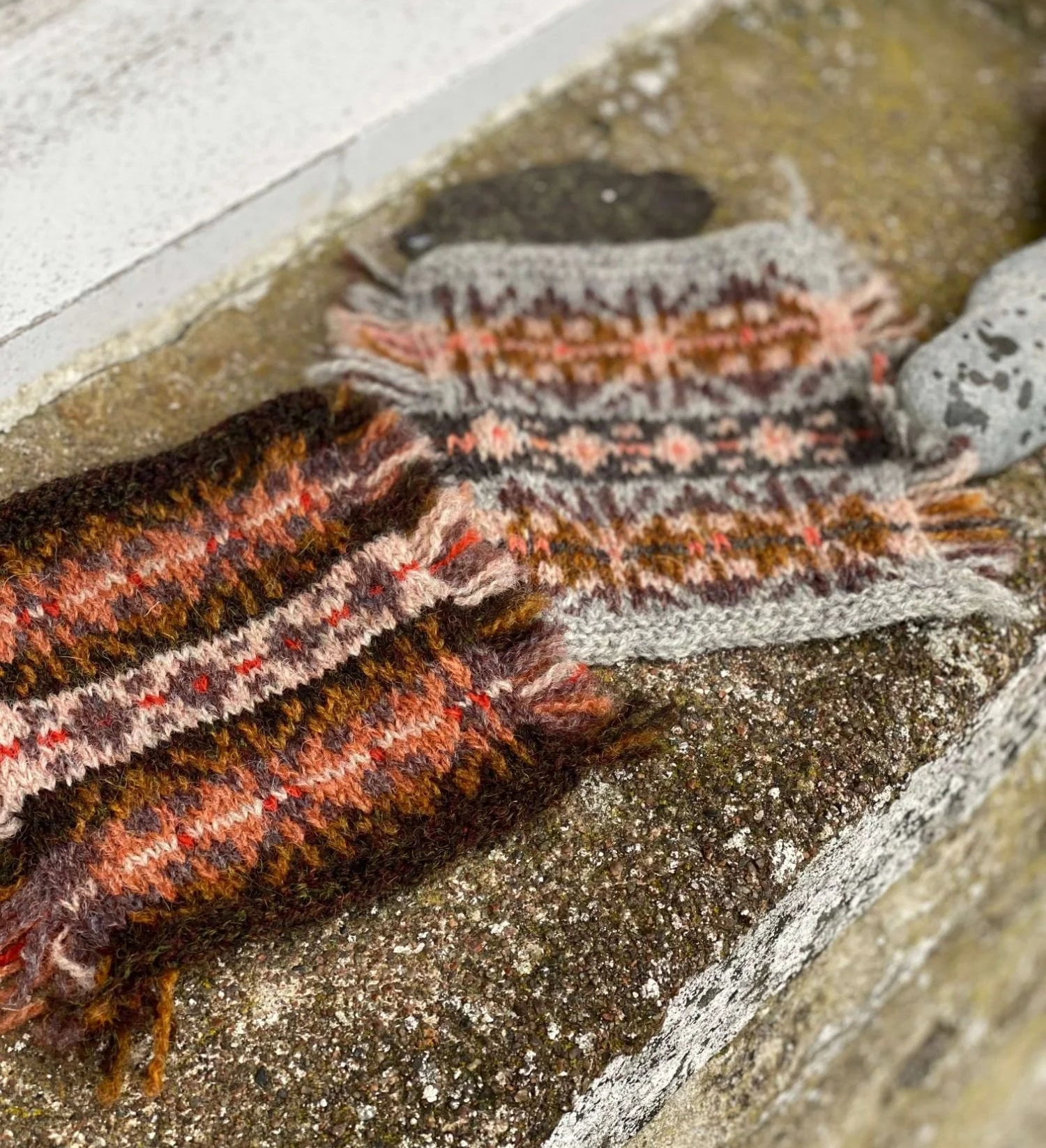 Close-up of two knitted colorwork swatches on a stone window ledge.
