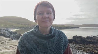 Gudrun Johnston sitting outside in Shetland on rocky terrain next to the sea.